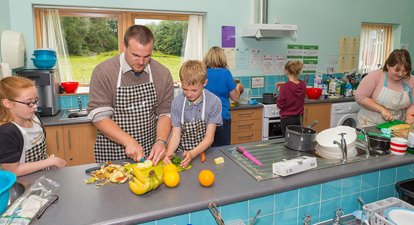 Home Economics teacher and pupils wearing aprons and chopping fruit in kitchen