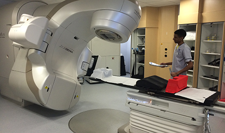 A QMU student standing beside a Radiotherapy machine
