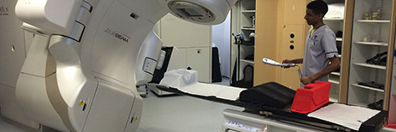A QMU student standing beside a Radiotherapy machine