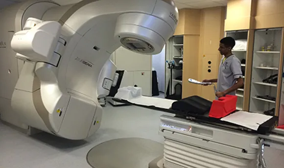 A QMU student standing beside a Radiotherapy machine