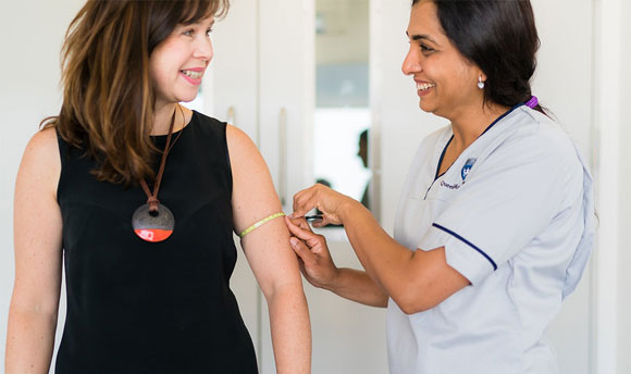 A nurse smiling with a woman whilst measuring her upper arm