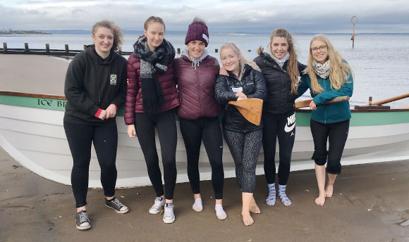 Student rowing team posing for a photo by their boat