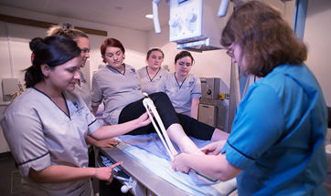 Radiography students holding a model shin bone beside a student's leg