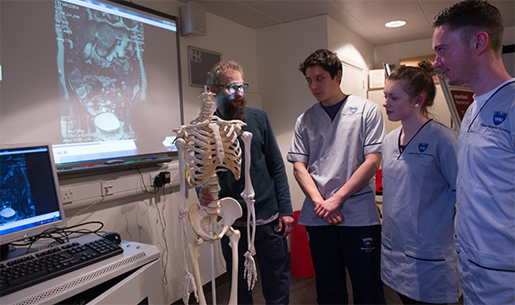 Radiography students with their lecturer looking at a model skeleton