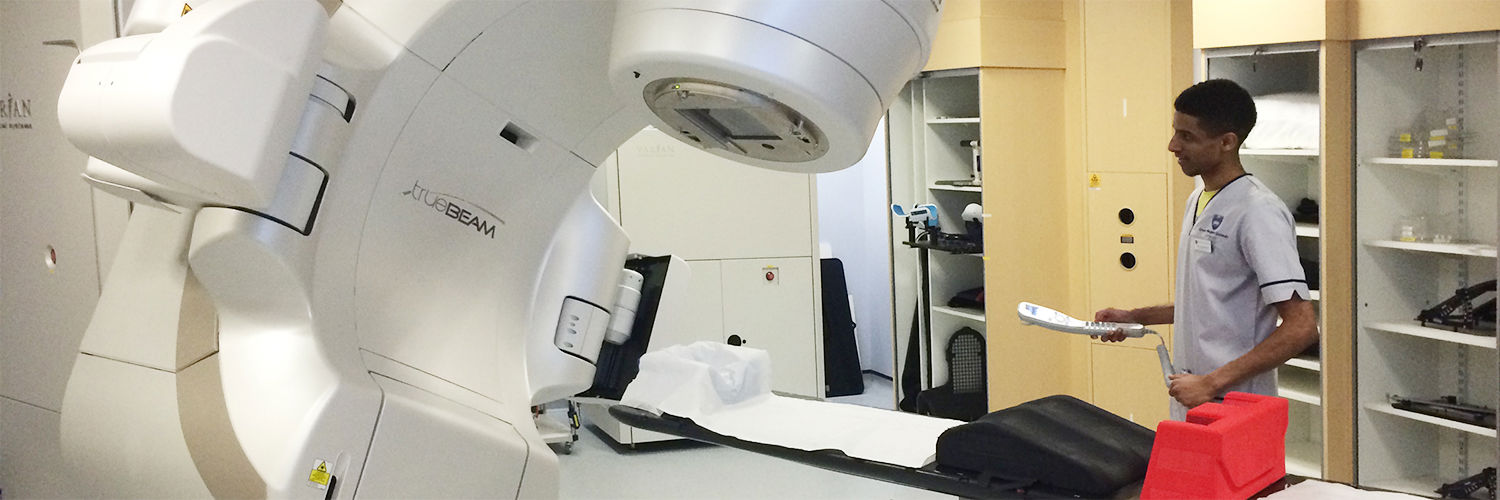 A QMU student standing beside a Radiotherapy machine
