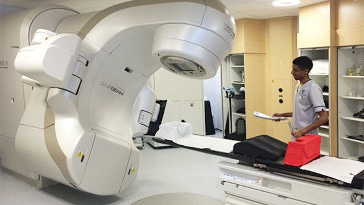 A QMU student standing beside a Radiotherapy machine