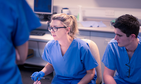 A student in blue scrubs looking at something intently out of shot