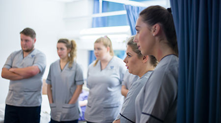 A row of QMU student nurses listening intently as a senior nurse speaks to them