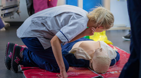 Queen Margaret University Nursing Student kneeling over a Resusci Annie doll