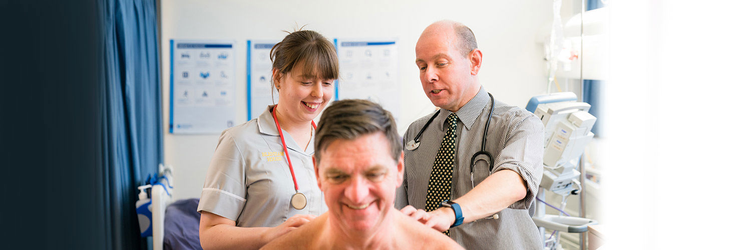 A student nurse with a doctor examining a patient's back while they all smile