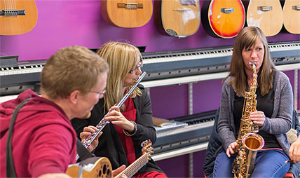 A group of people in a music shop playing a saxophone, a flute and a guitar