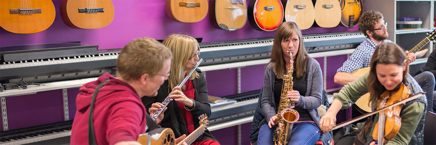 A group of people in a music shop playing a saxophone, a flute and a guitar