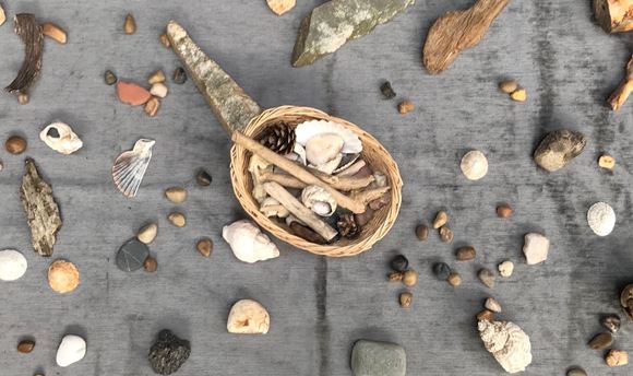 A grey blanket covered in stones and seashells with a basket in the centre