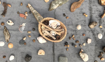 A grey blanket covered in stones and seashells with a basket in the centre