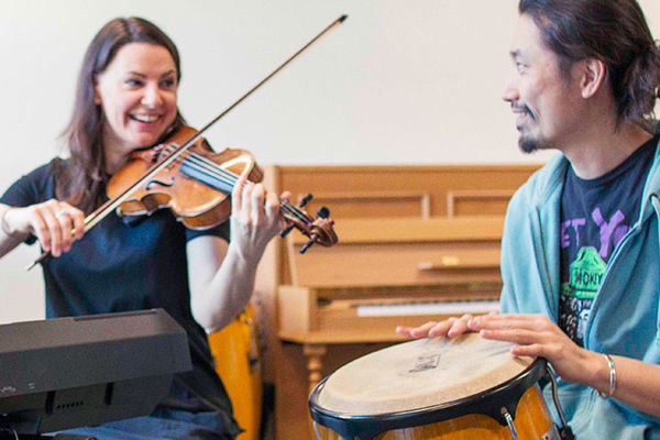 A smiling violinist and a drummer playing a bongo
