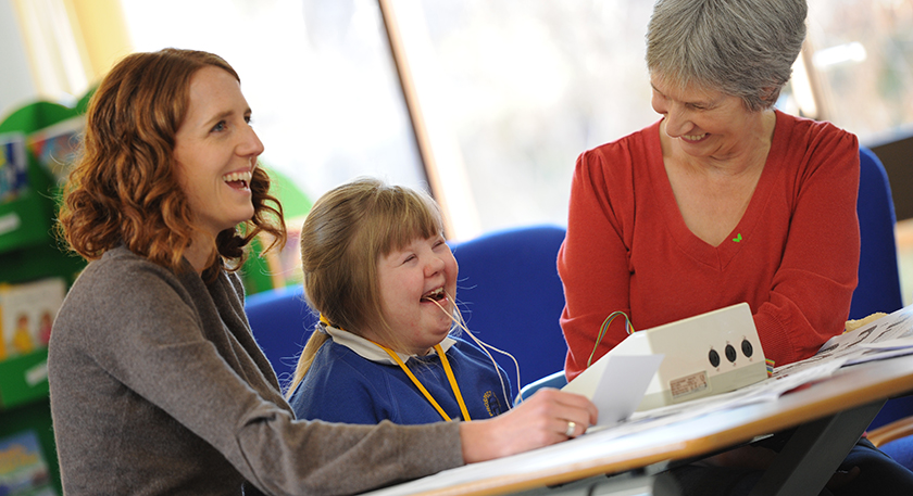 A young girl with Downs Syndrome using the speech and language therapy equipment with two adults