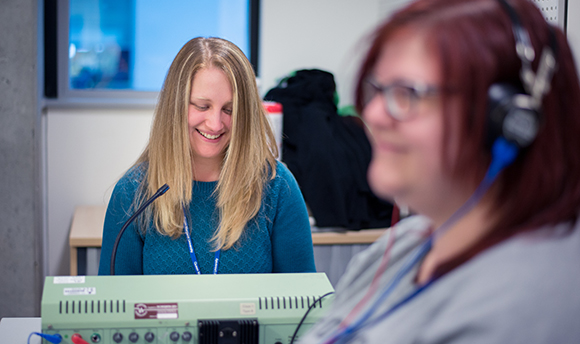 A woman with a headset on and a women behind her sat at a desk