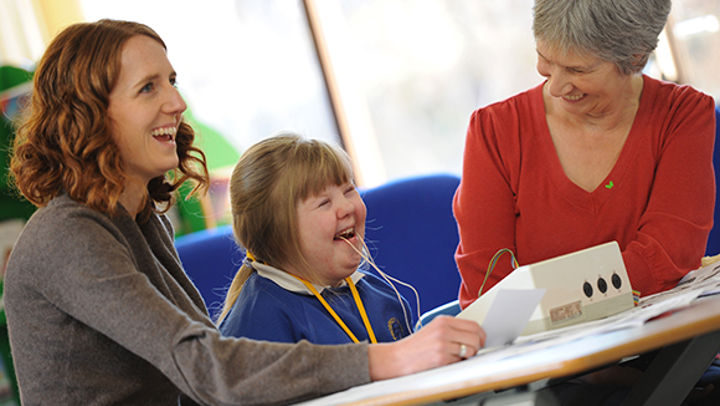 A young girl with Downs Syndrome using the speech and language therapy equipment with two adults