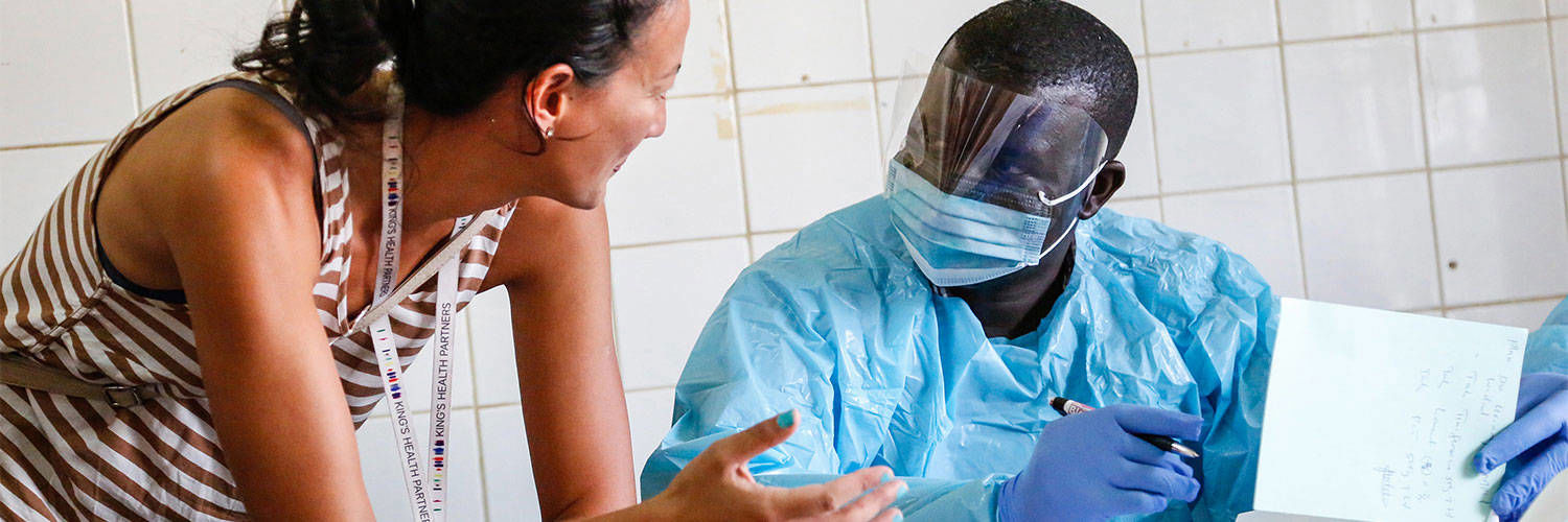 A woman leaning onto a table to talk to one of the nurses who is wearing full PPE