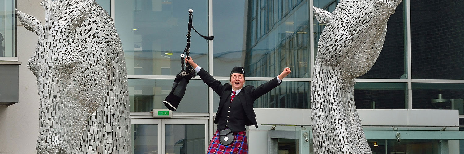 A piper posing by the Kelpies replica at QMU Edinburgh