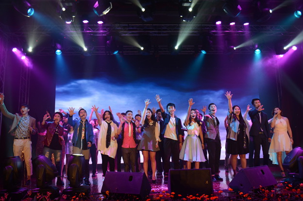 A stage filled with performers singing with their hands raised to the sky