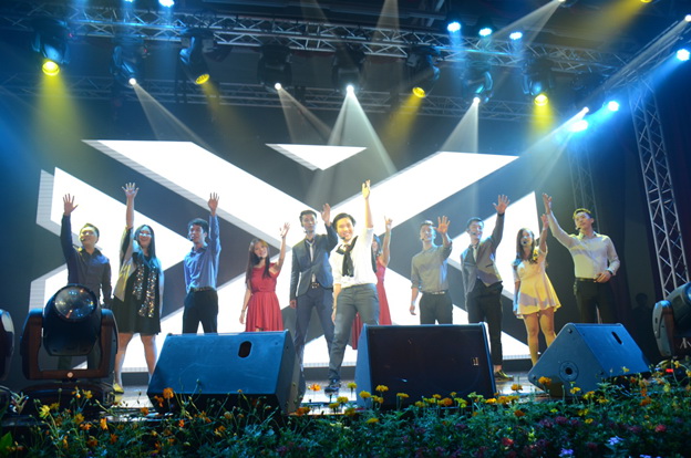 A stage filled with performers singing with their hands raised to the sky