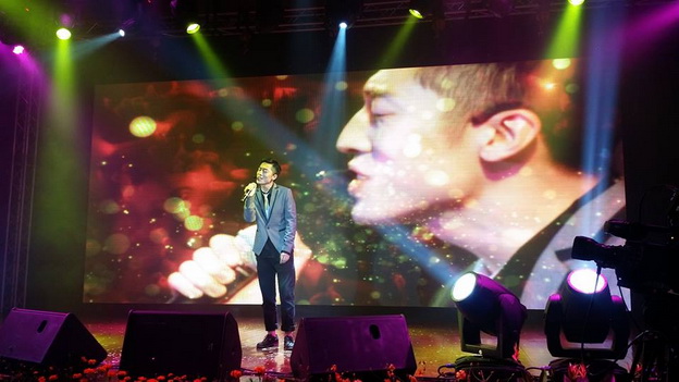 A performer singing on a stage with a close up video of them playing on the screen behind them