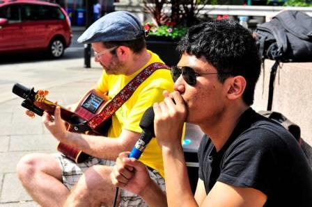 Two buskers playing guitar and singing outside on a sunny day