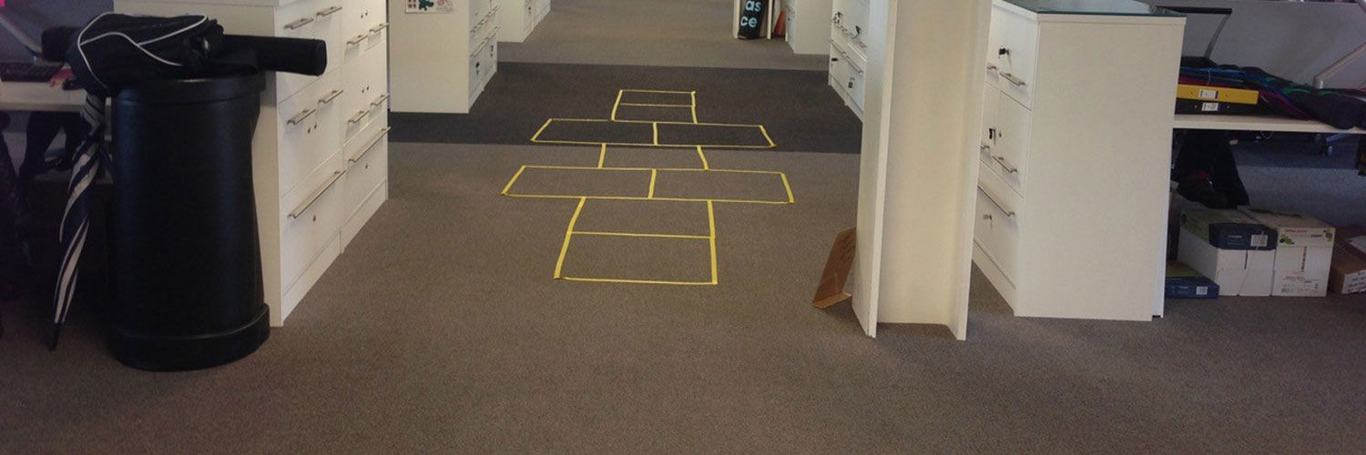 A hopscotch latter made of yellow sellotape on an office floor