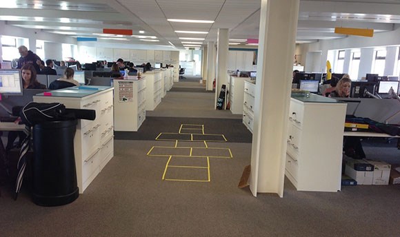 A hopscotch latter made of yellow sellotape on an office floor
