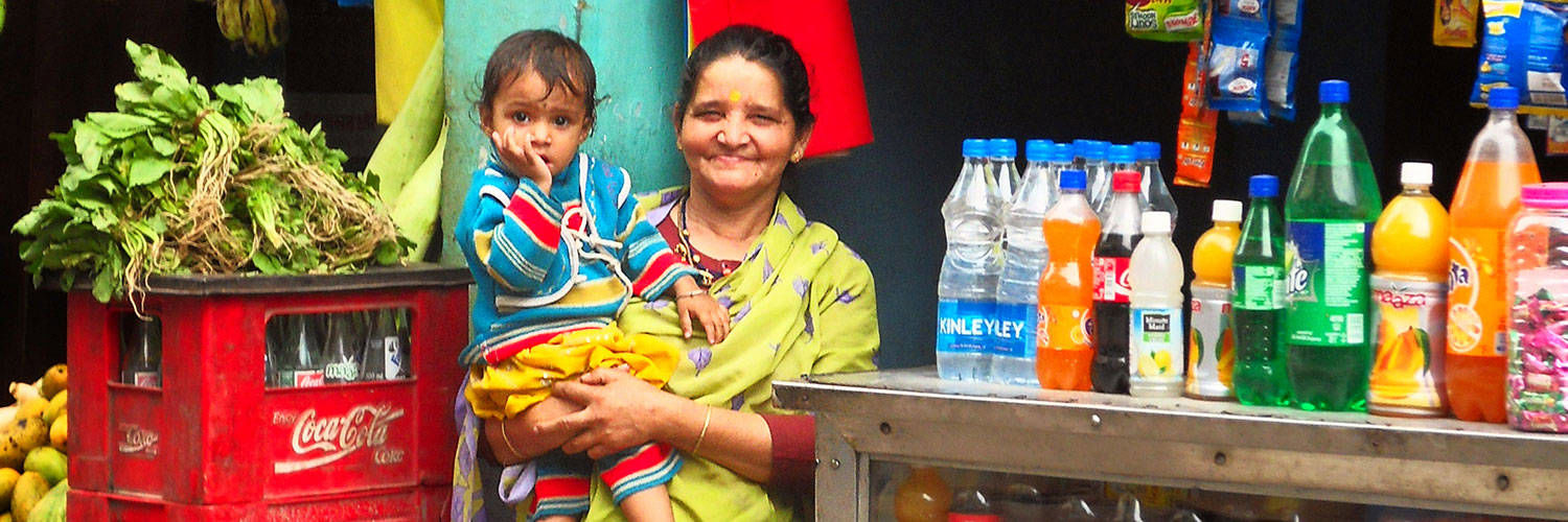 An Indian woman smiling and holding a young child at a grocery stall