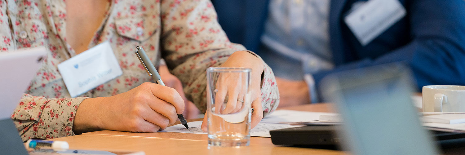 A woman in a floral top writing on a piece of paper