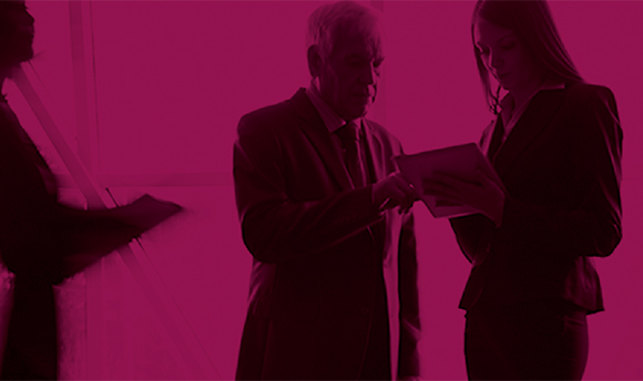 A black and pink photo of two professionals looking at paperwork as blurry people walk around them