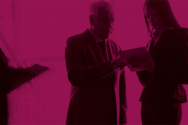 A black and pink photo of two professionals looking at paperwork as blurry people walk around them