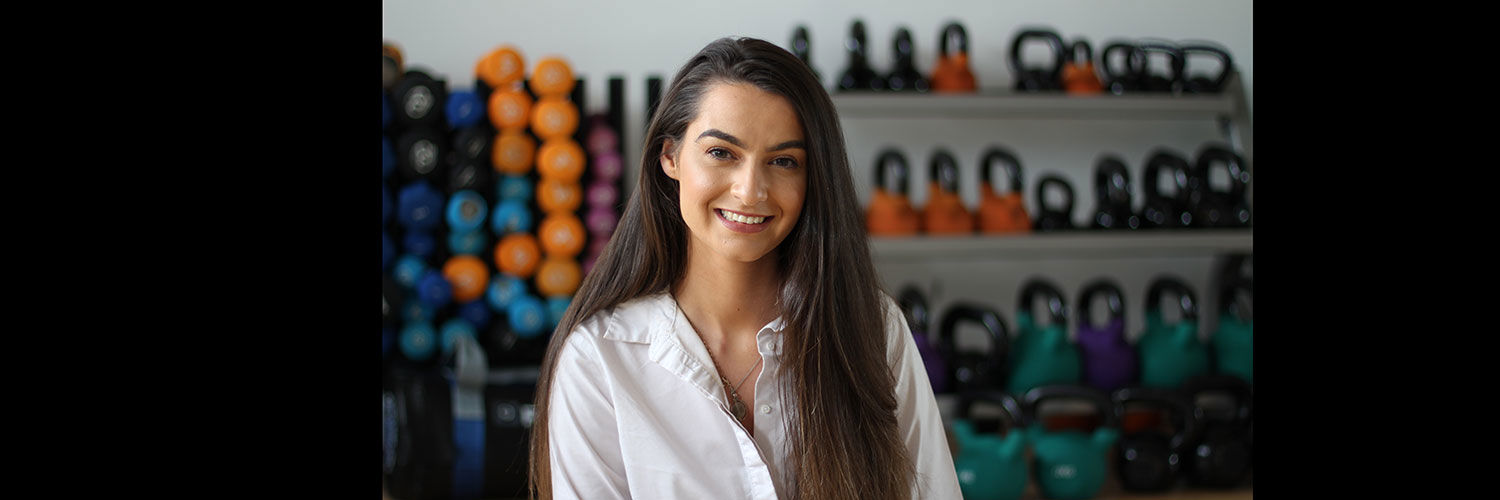 A young brunette woman in a gym beside the kettlebells and weights