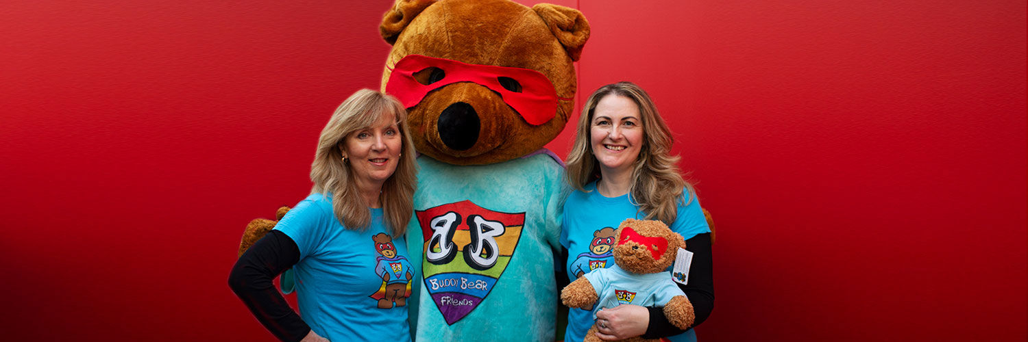 Two smiling women next to someone in a large bear costume