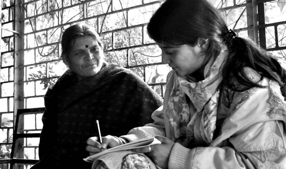 A Hindu woman talking to a younger girl who is taking notes