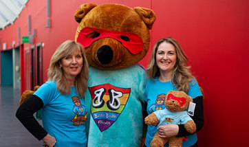 Two smiling women next to someone in a large bear costume