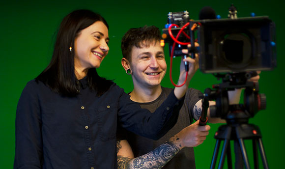 Two QMU students with a professional camera in front of a green screen