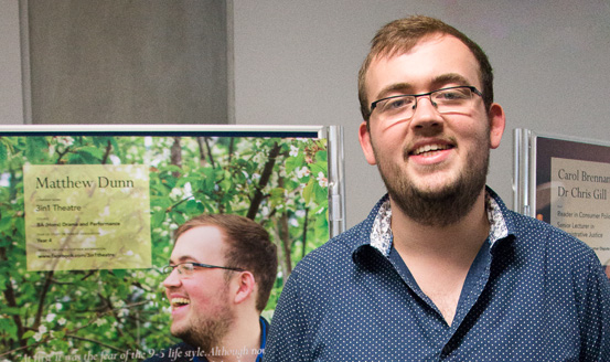 Matthew Dunn smiling by a poster with him on it