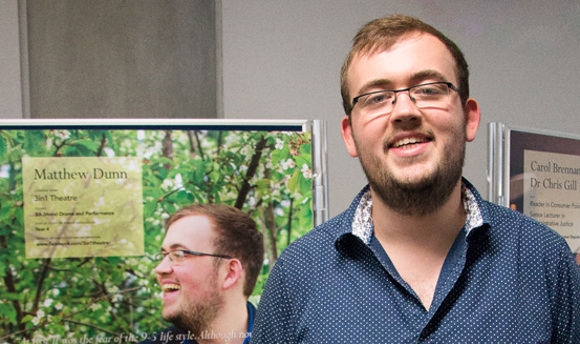 Matthew Dunn smiling by a poster with him on it
