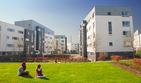 Two students sitting on the grass outside the QMU student village on a sunny day
