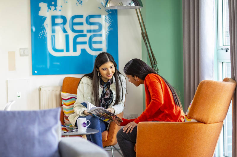 Two QMU students sitting under a ResLife sign