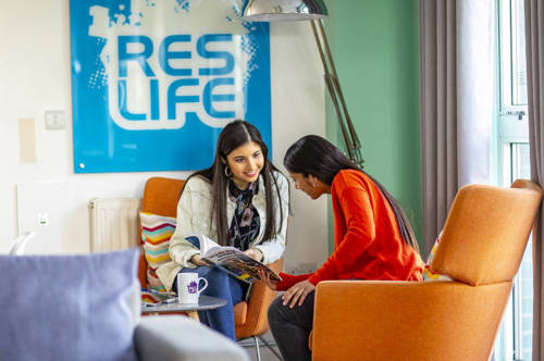 Two students talking and reading a magazine in QMU accommodation common area