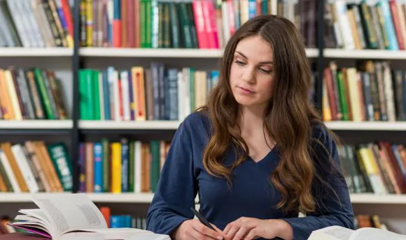 Student taking notes from books in library