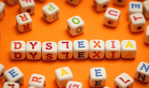 dyslexia spelled out with letters on small cubes over an orange background 