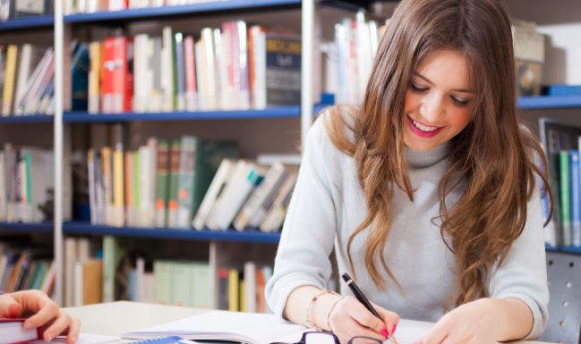 Student taking notes from books in library