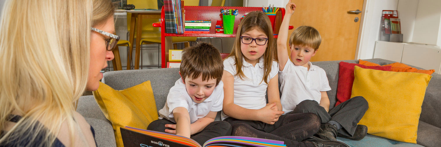 Three young children are being shown a science education book from their teacher.