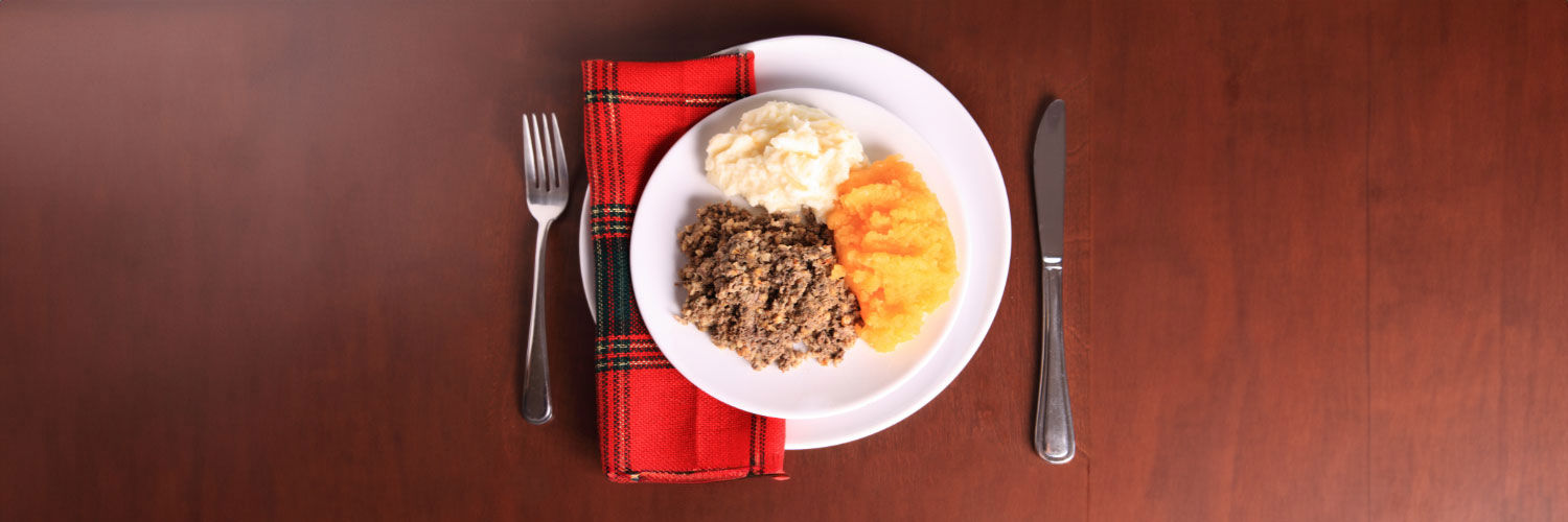A haggis supper on a plate, accompanied by a tartan napkin.