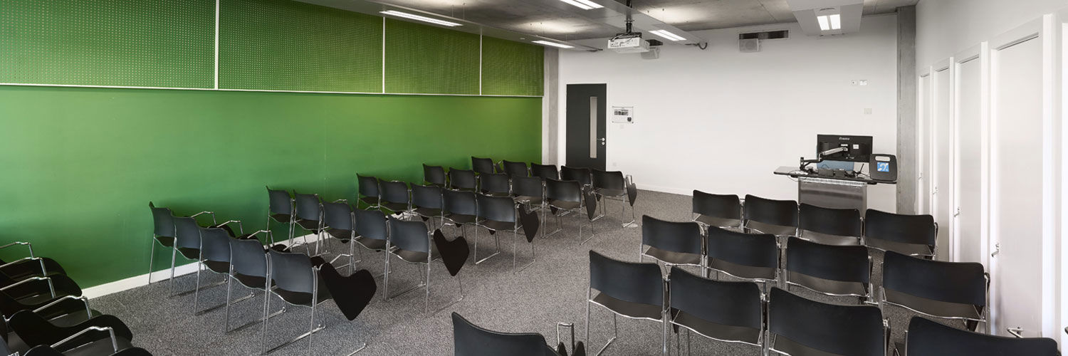 The interior of one of QMU's classrooms. There are several rows of black chairs with fold-down tables facing towards the front of the room.